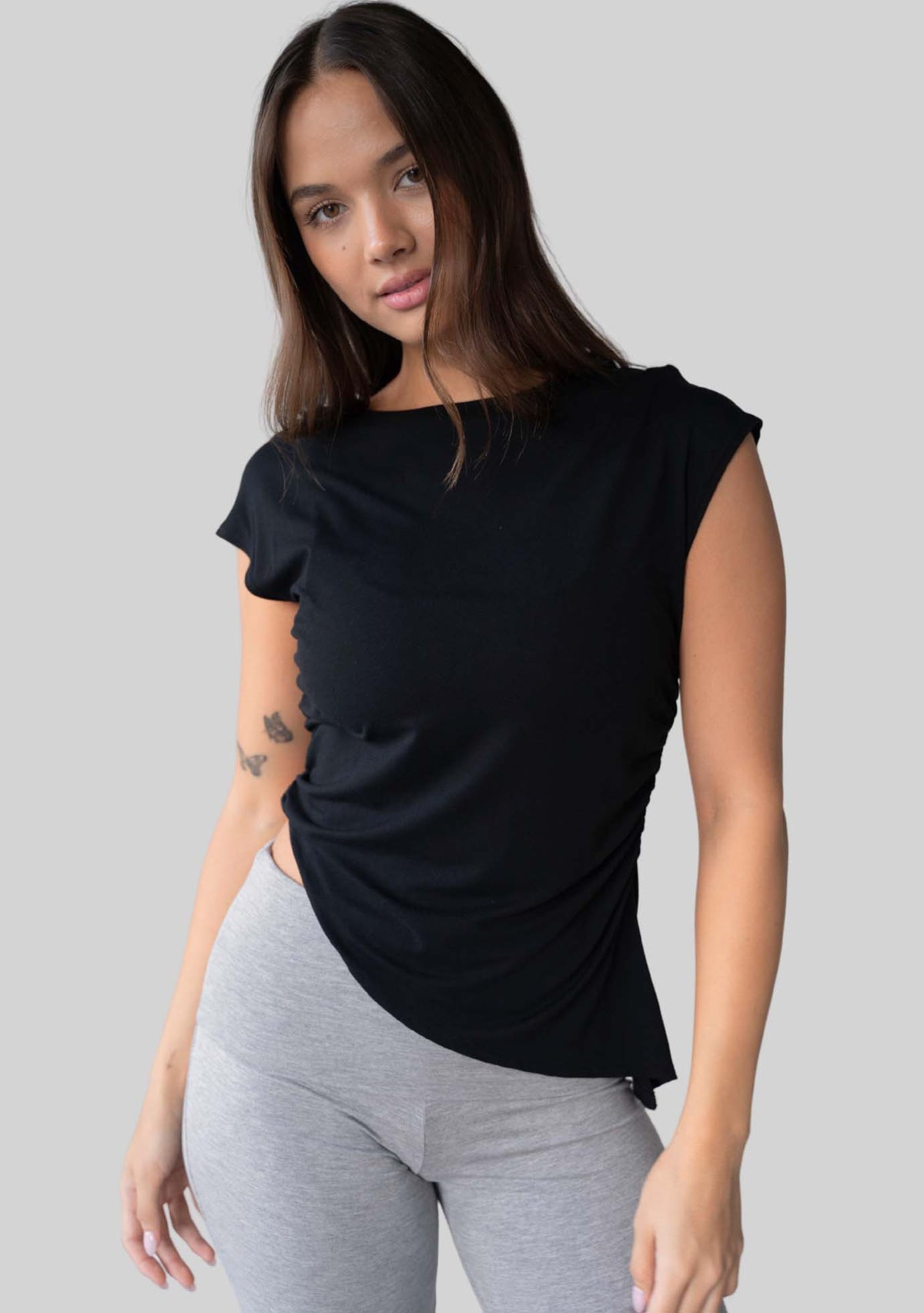 Model wearing the JALA Align Tee in Black with side shirring and an asymmetrical hem, front view