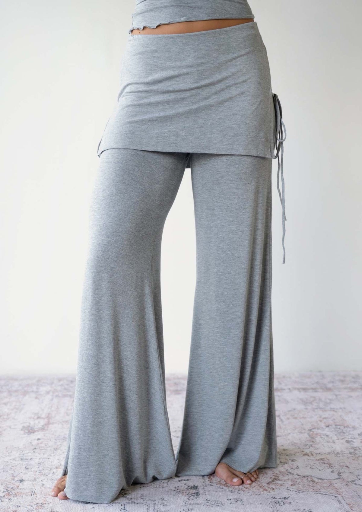 Model wearing the JALA Luna Pant in Heather Grey with skirt overlay and side ties, front view
