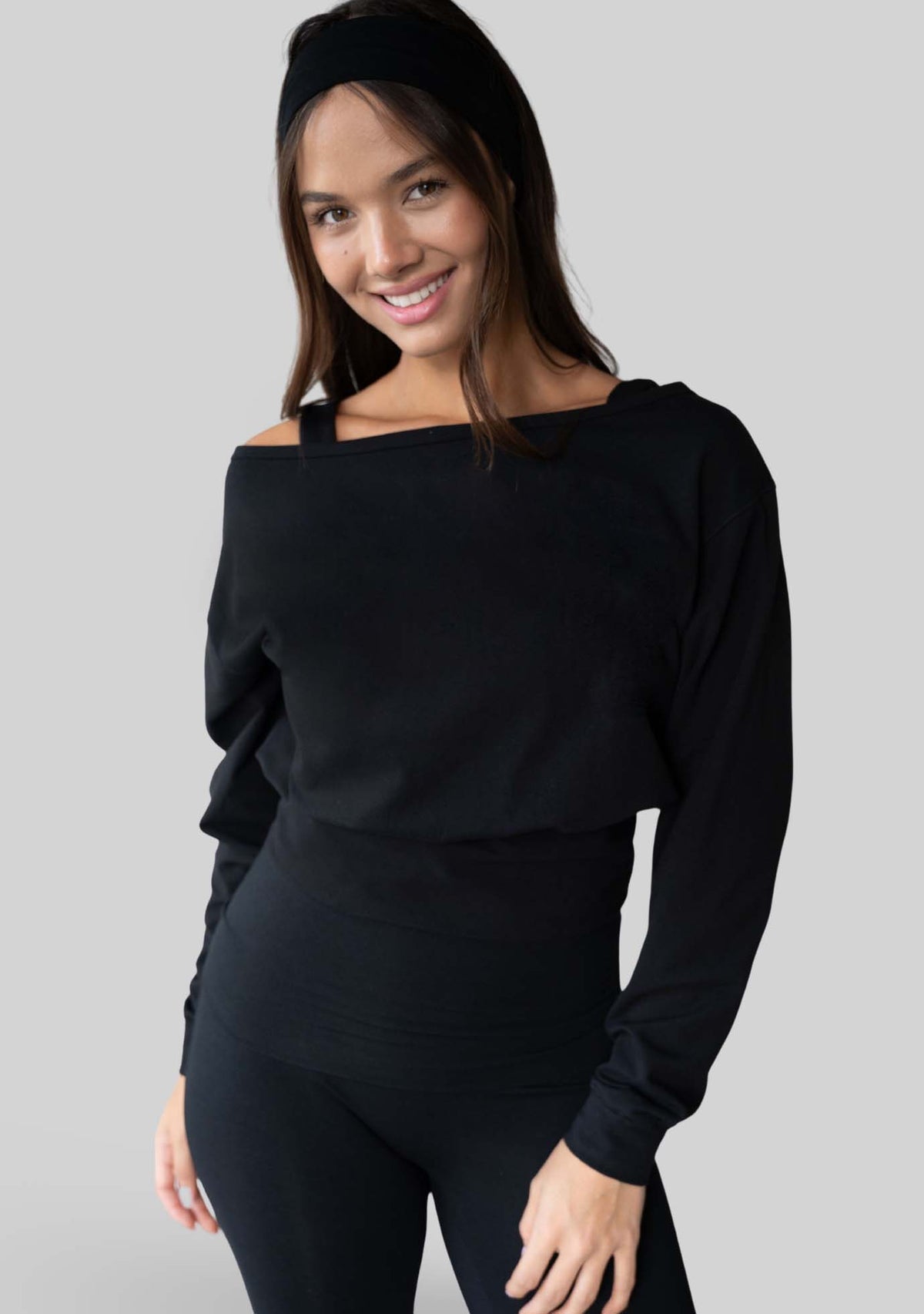 Model wearing the JALA Aela Top in Black, an off the shoulder long sleeve top, front view. [label] Leah is 5'7" XS