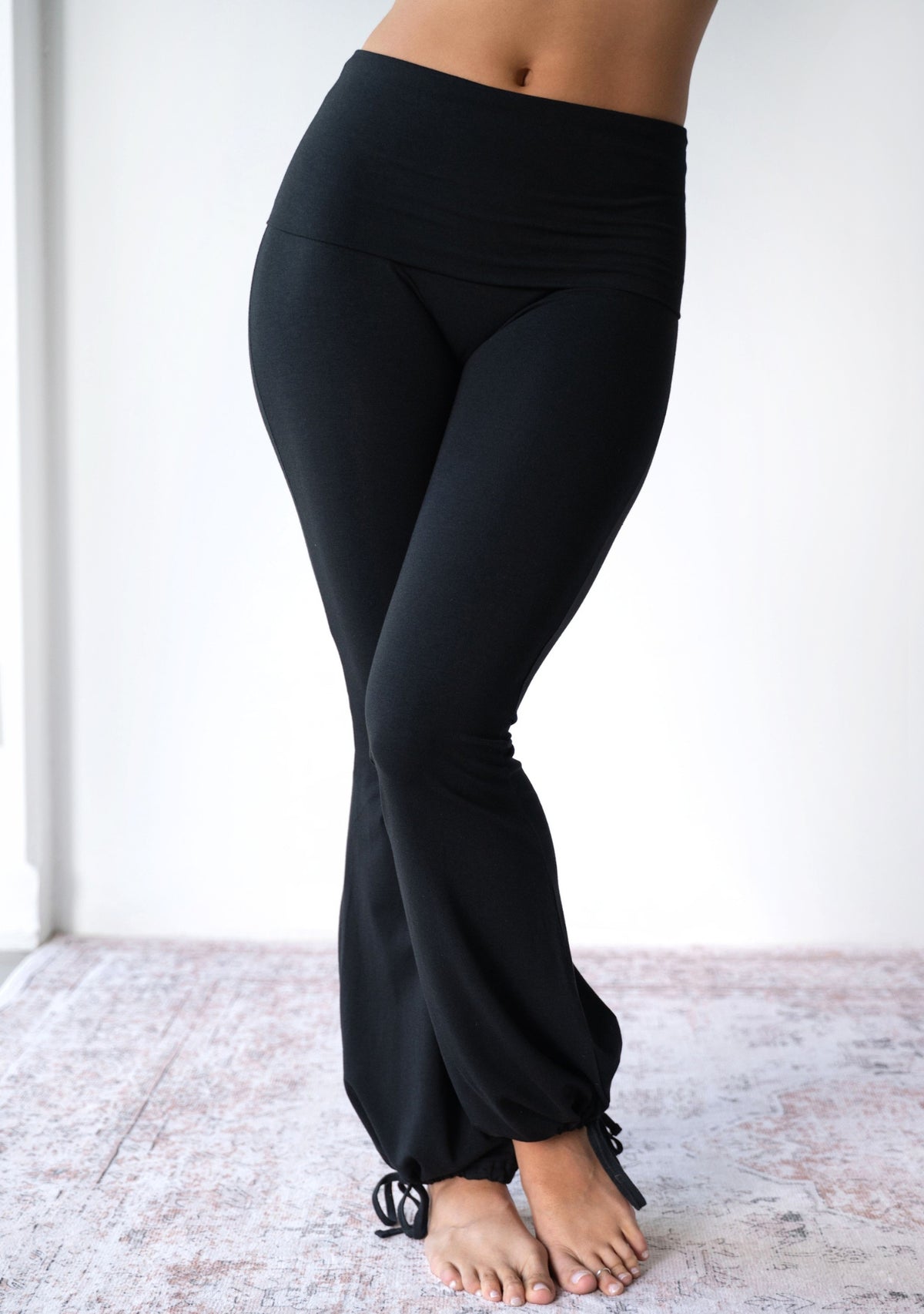 Model wearing the JALA Nama Balloon Flare Legging in Black with tie ankle balloon hem, front view. [label] Leah is 5'7" XS