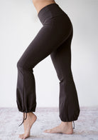 Model wearing the JALA Nama Balloon Flare Legging in Chocolate with tie ankle balloon hem, side view. [label] Leah is 5'7" XS