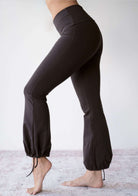 Model wearing the JALA Nama Balloon Flare Legging in Chocolate with tie ankle balloon hem, side view. [label] Leah is 5'7" XS